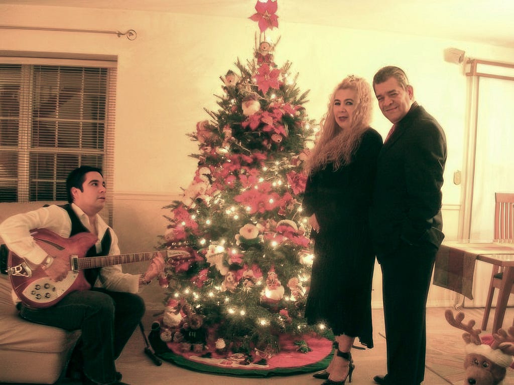 Juan playing guitar by the Christmas tree while his parents look on