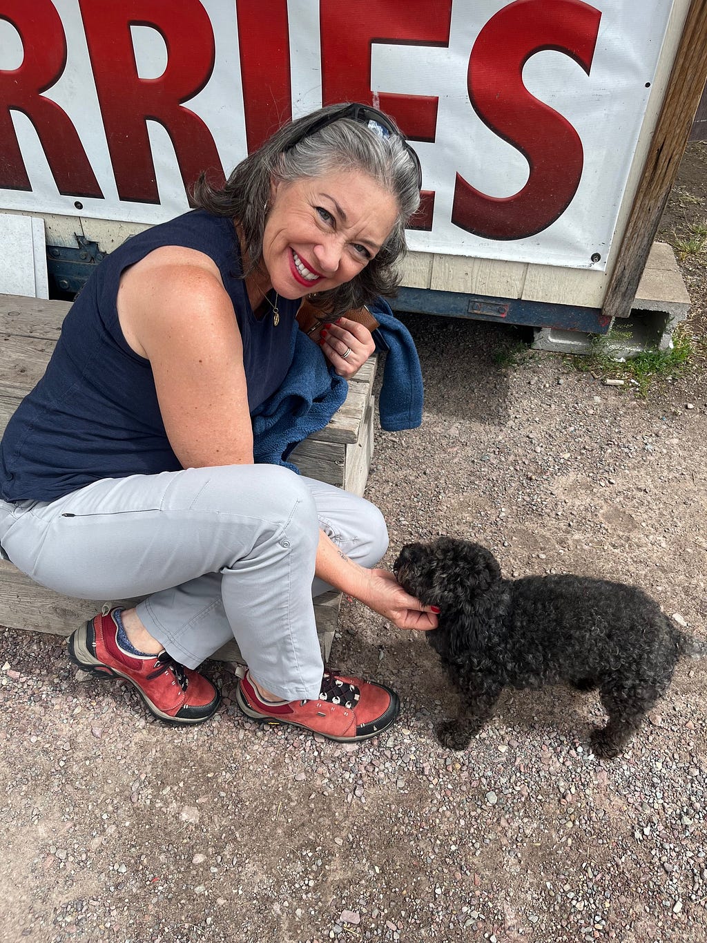 A beautiful smiling woman scratches under the chin of a small black dog