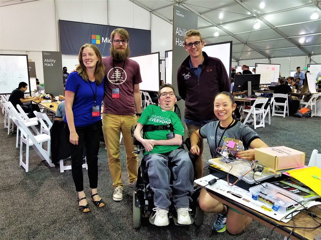 Inside the Hackathon tent, a team of five researchers, designers, and engineers pose with a prototype, all smiles.