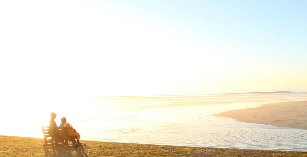 An old couple at sunset, having navigated life’s transitions, is still committed after a lifetime of relationship building.