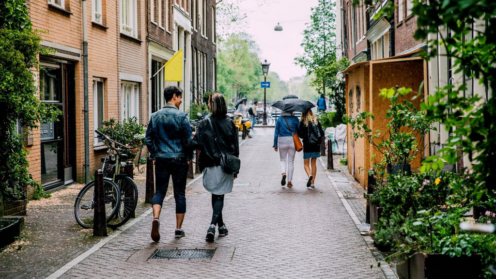 People strolling along a street sandwiched between buildings.