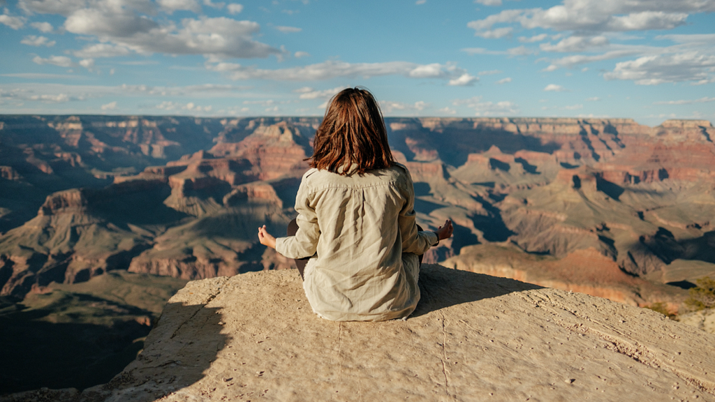 Photo of woman meditating on a mountain with view of sky and mountains