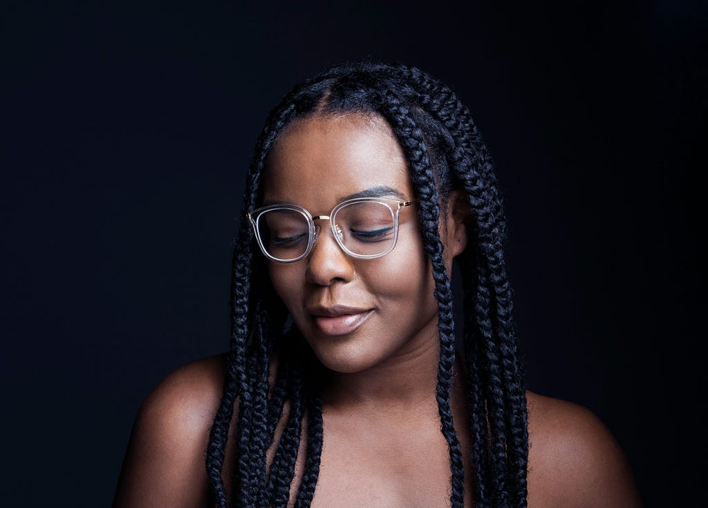 Black woman with braided hair wearing glasses and looking down.