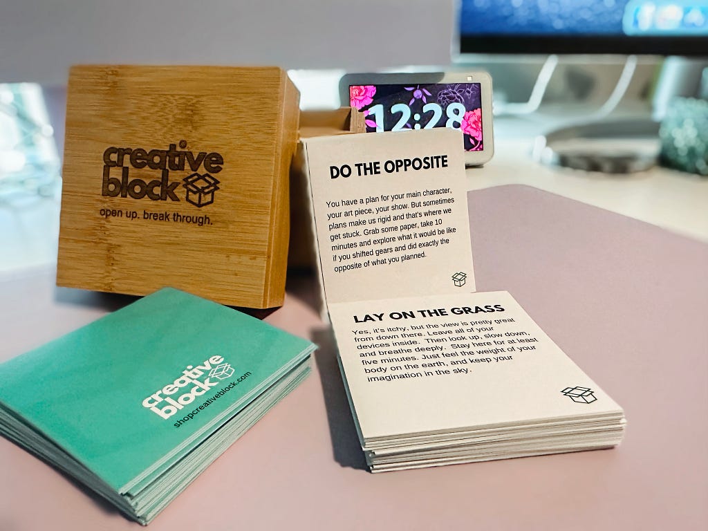 A photo of the Creative Block deck. On the left if the wooden box it comes in, with some of the cards standing next to it on the right and laying down in front of it.