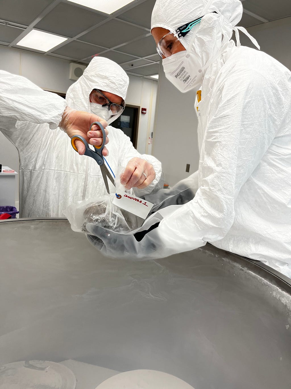 Two researchers wearing protective gear are cutting open a bag labeled “Omnivore 1” over an icy freezer container.