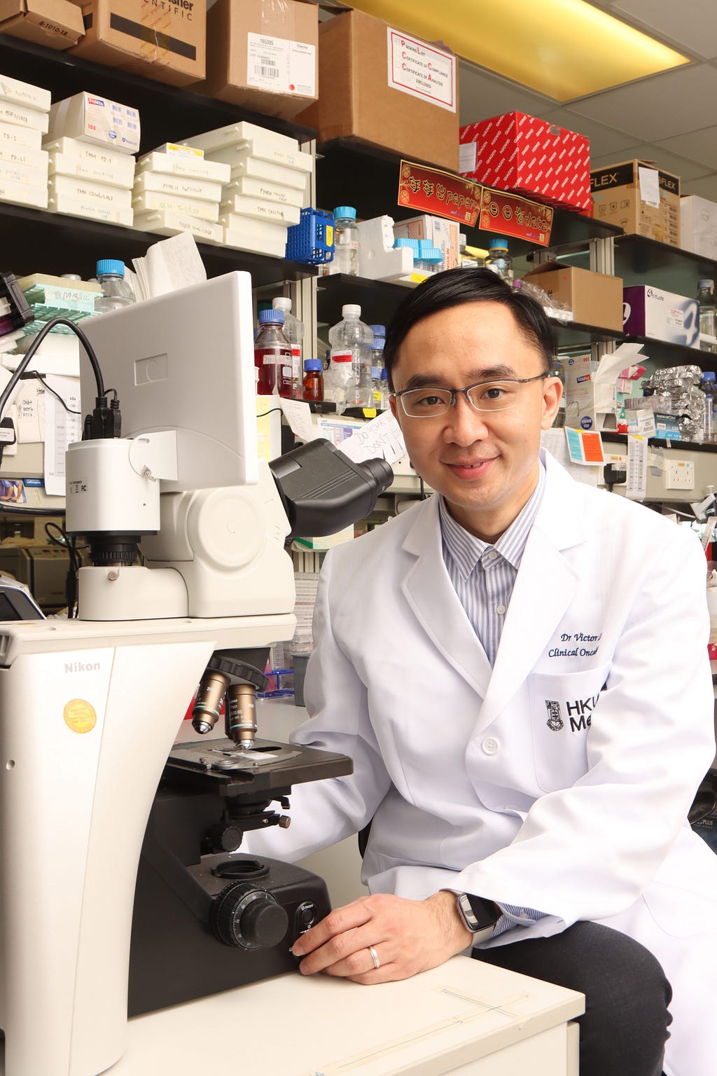 Dr Victor Lee Ho-fun, sitting in front of a microscope, smiles to the camera in a wet lab.