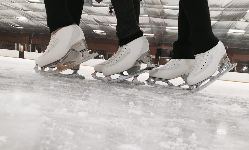 Close-up of three sets of figure skates on ice