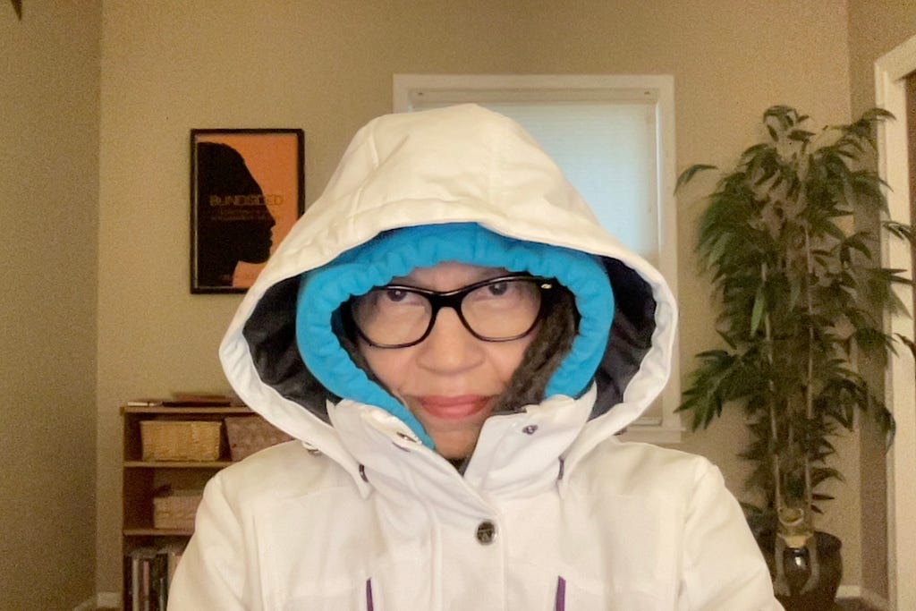 A woman bundled up in a down jacket and a hoodie frowns at the camera.