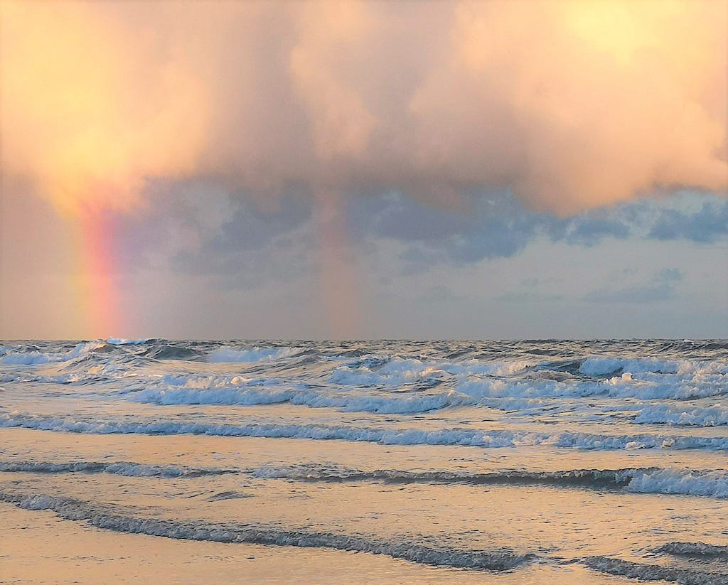A rainbow out at sea on the horizon.