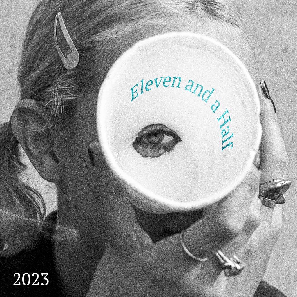 Cover photo, black and white closeup photo of girl holding and looking through a hole in a Styrofoam cup, Eleven and a Half printed on the inside of the cup