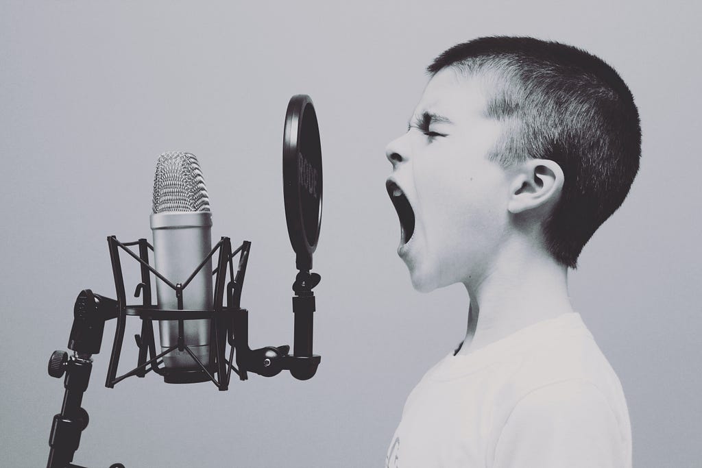 Immagine di un bambino che parla a voce alta davanti a un microfono nel tentativo di far sentire la propria voce