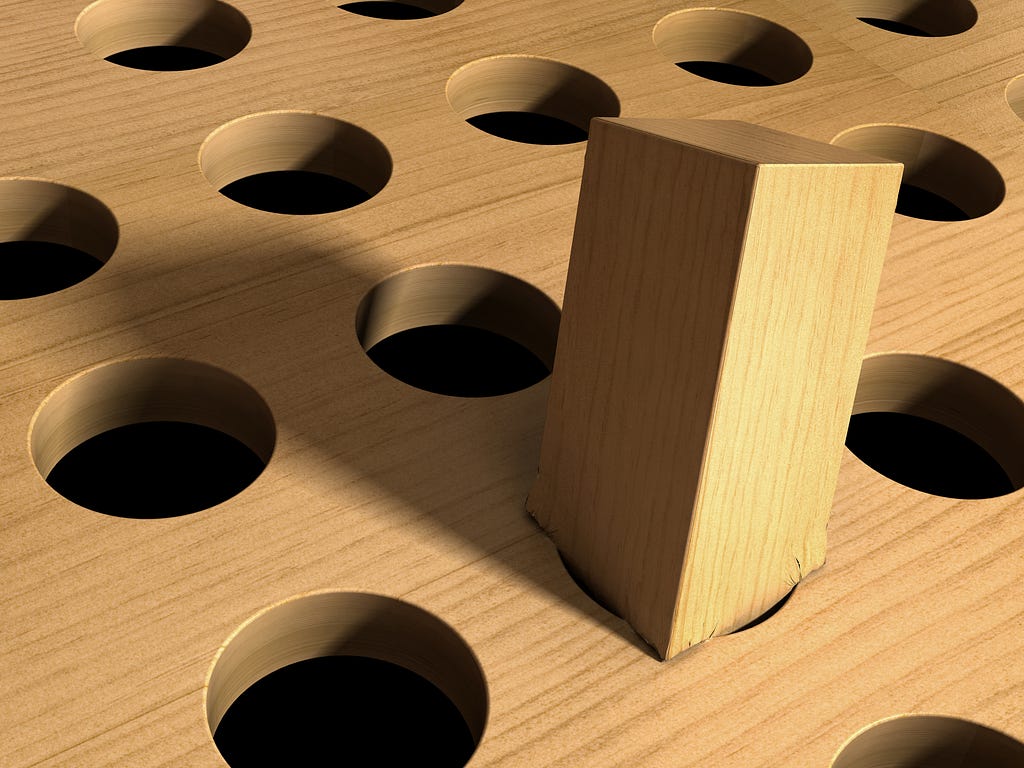A close up of a square peg, damaged as it sits atop a round hole.