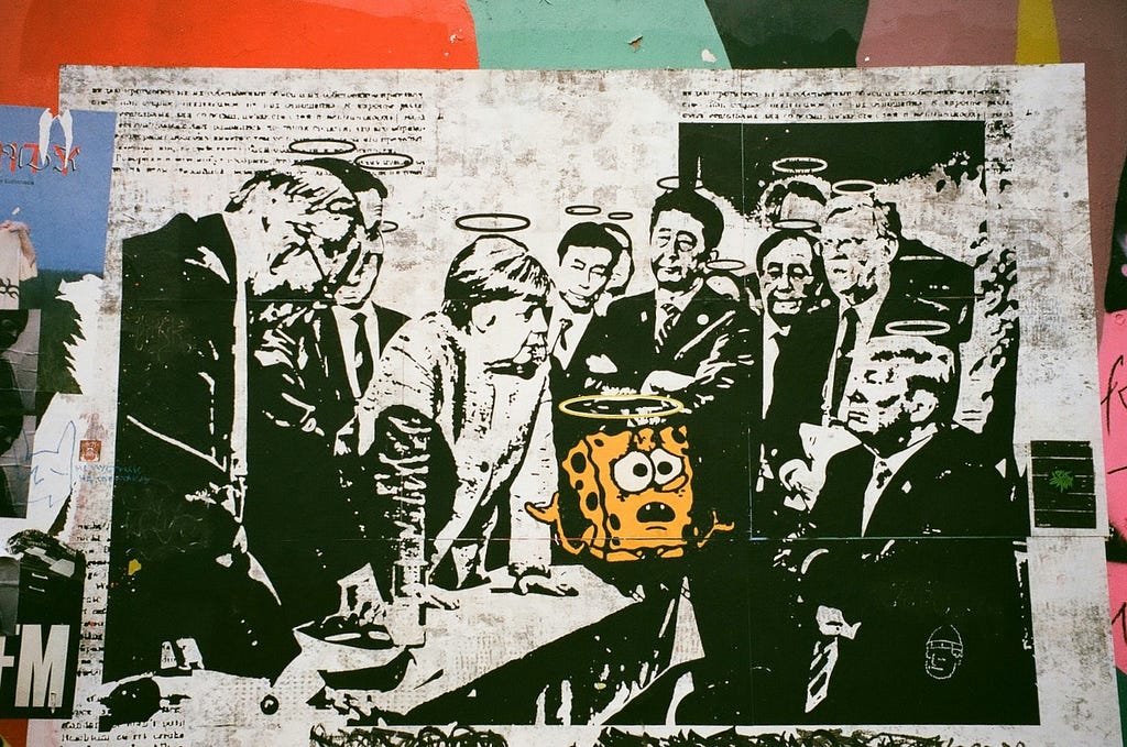 A historical picture of a meeting of top global leaders, removed and bleached of the pictures natural colors; inserted in is Sponge Bob with his normal coloring but a little more deep yellow. All in the pictures have halos above their heads. The leaders look tense, with former Prime Minster, Angela Merkel leaning forward upon the table while Fmr. President Trump has his arms folded across his chest.