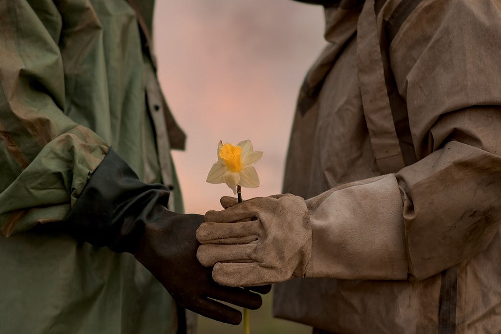 A man and a woman in a chemical protection suit. Post-apocalypse. A man gives a flower to his woman.