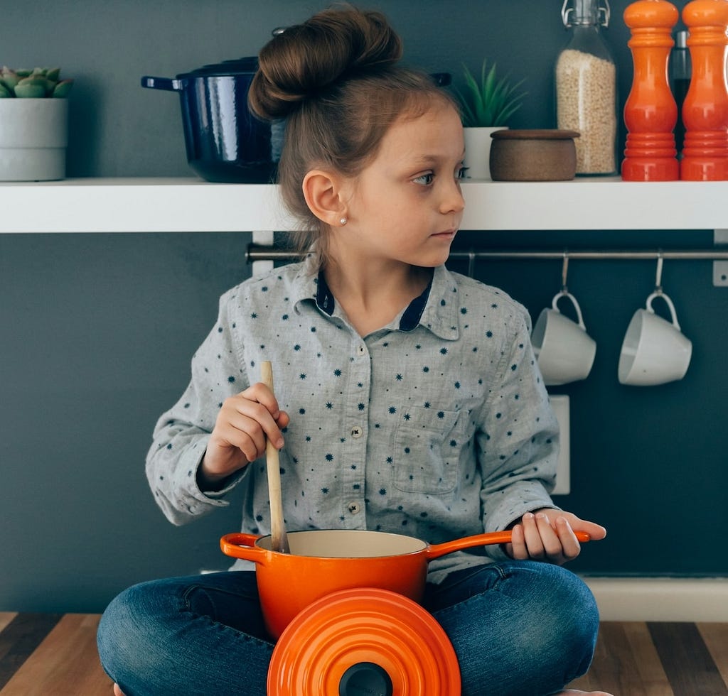 A young girl stirring an orange pot.