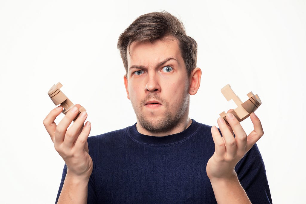 Attractive 25 -30 year old business man looking confused with wooden puzzle.