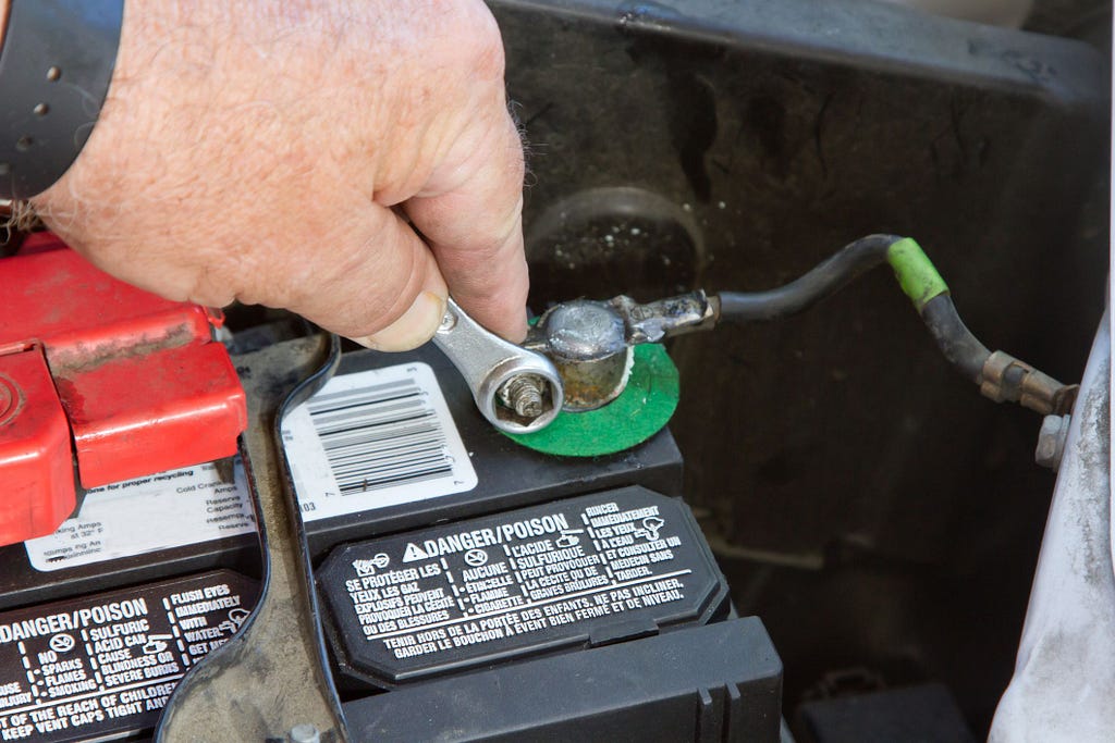 Person disconnecting the negative terminal of a car battery.