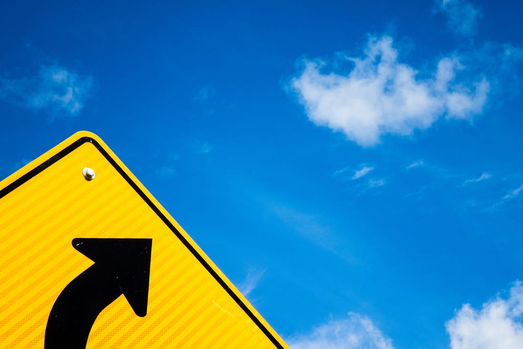 Yellow street sign pointing to a bright blue sky