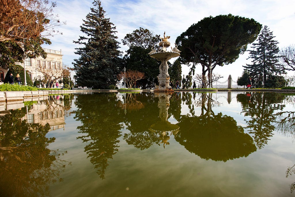 a pond with a water feature in the center in front of a palace