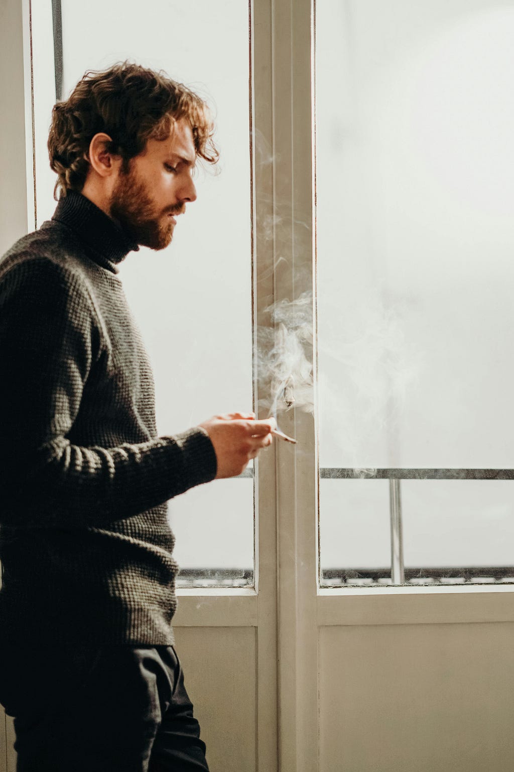 An adult smoking cigerette in tension near a full length window pane