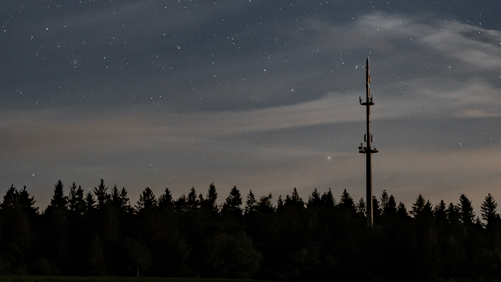 A radio tower alone in the woods at night.