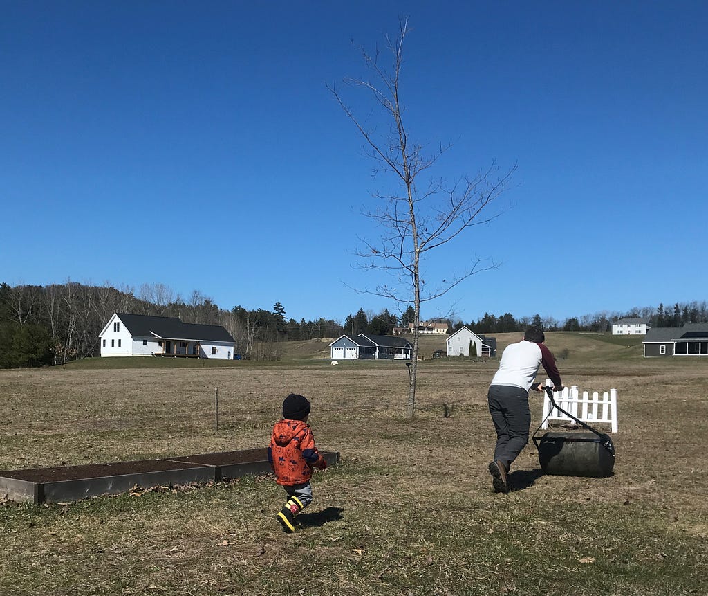 A child follows a few steps behind his father as the lawn is rolled, under a crystal clear blue sky