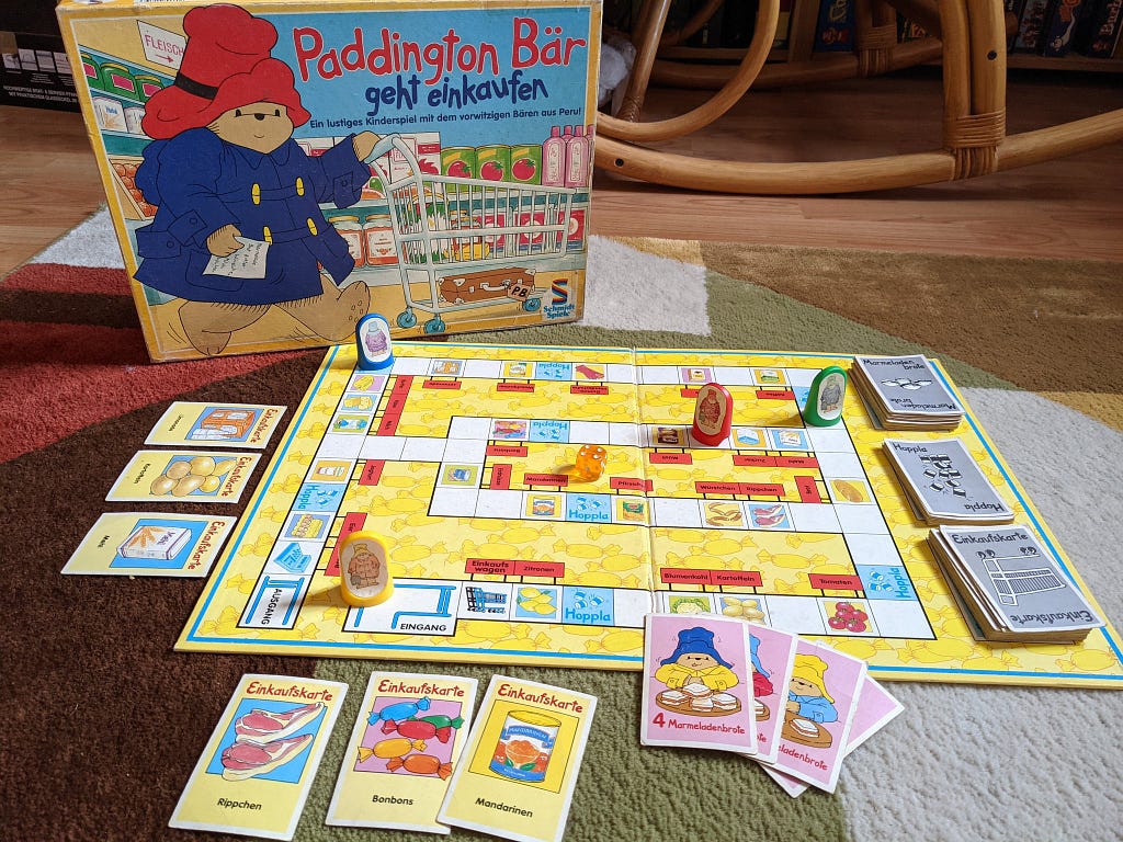 Spielaufbau des Schmidt Spieles “Paddington Bär geht einkaufen”. Zu sehen ist ein typisches Spielbrett mit aufgedeckten Karten, sowie offen liegenden Punkten. Figuren sind auf das Spielbrett platziert, um einen Testaufbau zu symbolisieren.