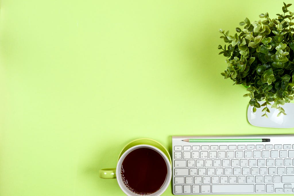 a plant, keyboard and cuppa all to the right of bright green background