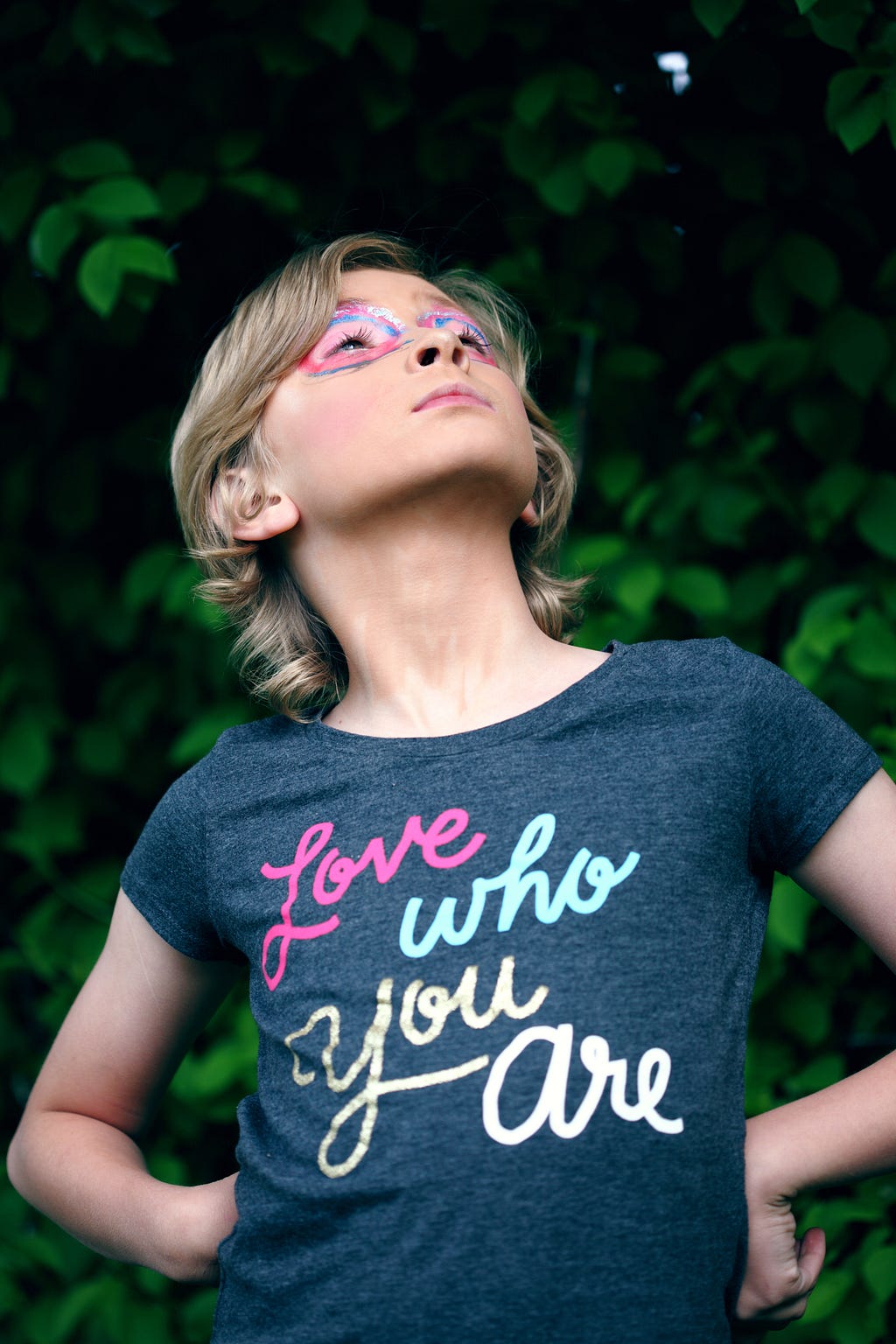 Photo of a nonbinary child with a shirt that states “Love who you are”