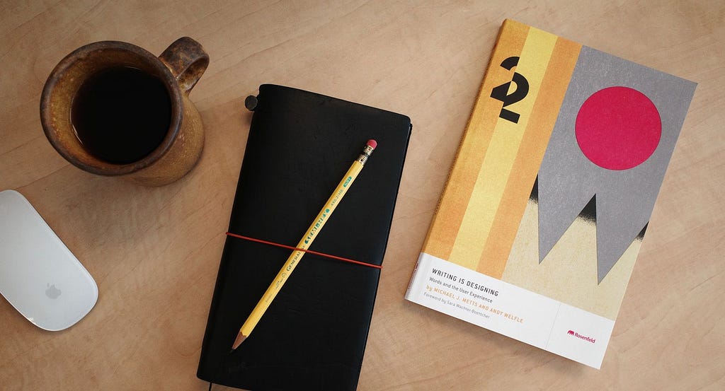 Photo of Writing is Designing with notebook, coffee cup, and computer mouse on a table.