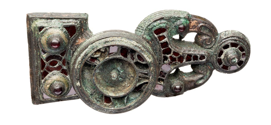 A decorated buckle dating from Swedish Vendel Period. Greenish and grey metal and red glass details.