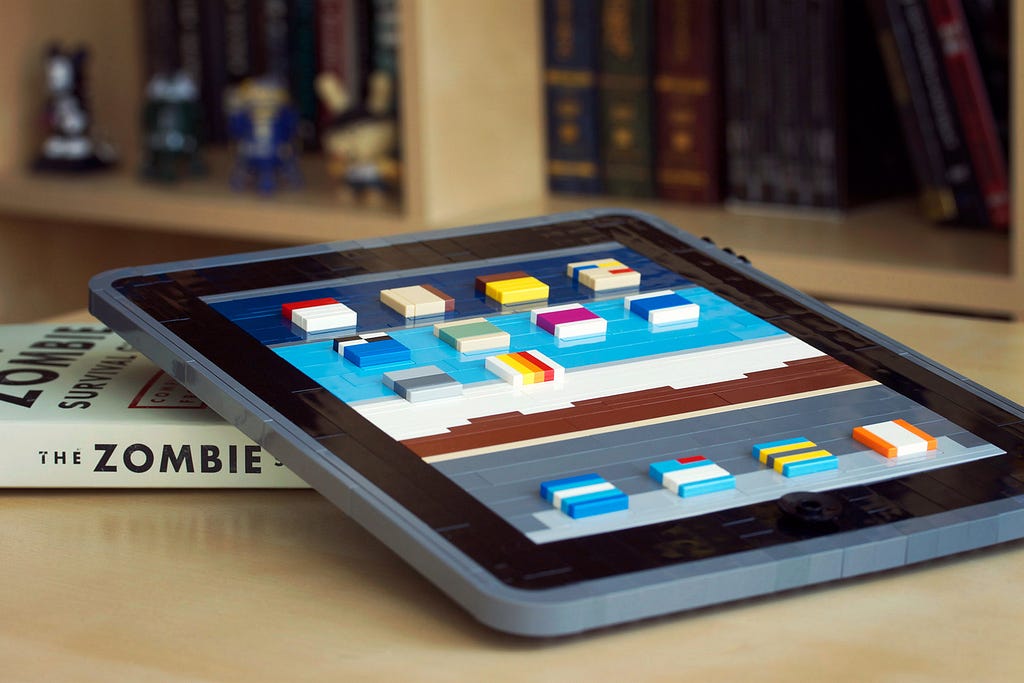 Um iPad totalmente construído com peças de Lego apoiado no livro The Zombie, sob o que parece ser um mesa com livro ao fundo.
