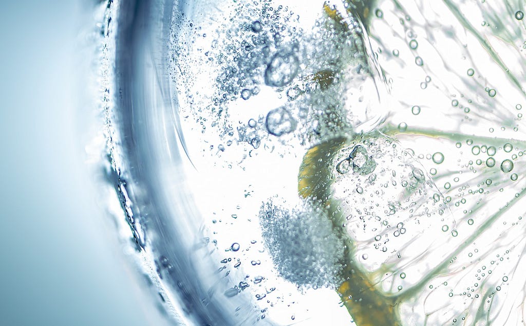 Close up of bubbles and a thin slice of lemon in a glass of sparkling water