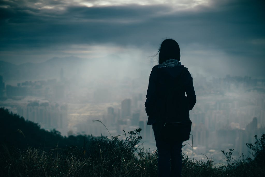 Shilouette of a person overlooking a city covered by fog and clouds.