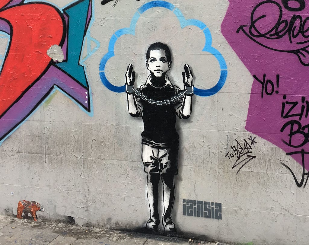Graffiti of a boy with his hands raised in handcuffs and a cloud outline encircling his head representing ideas.