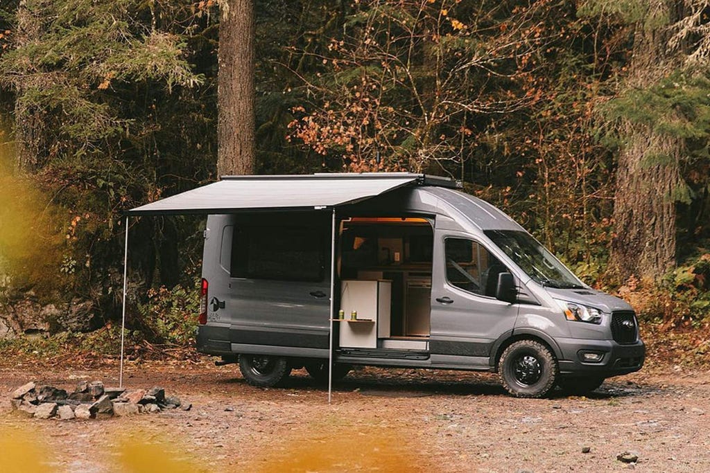 Grey Ford Transit camper with awning open in wooded area