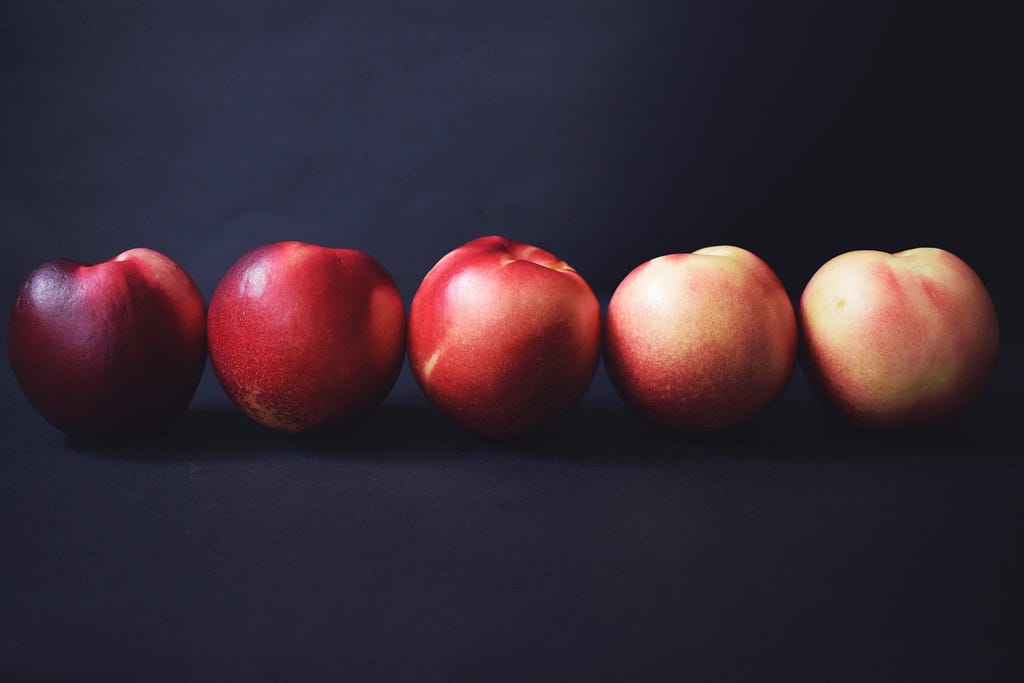 Five peaches lined up in a row, all touching each other.