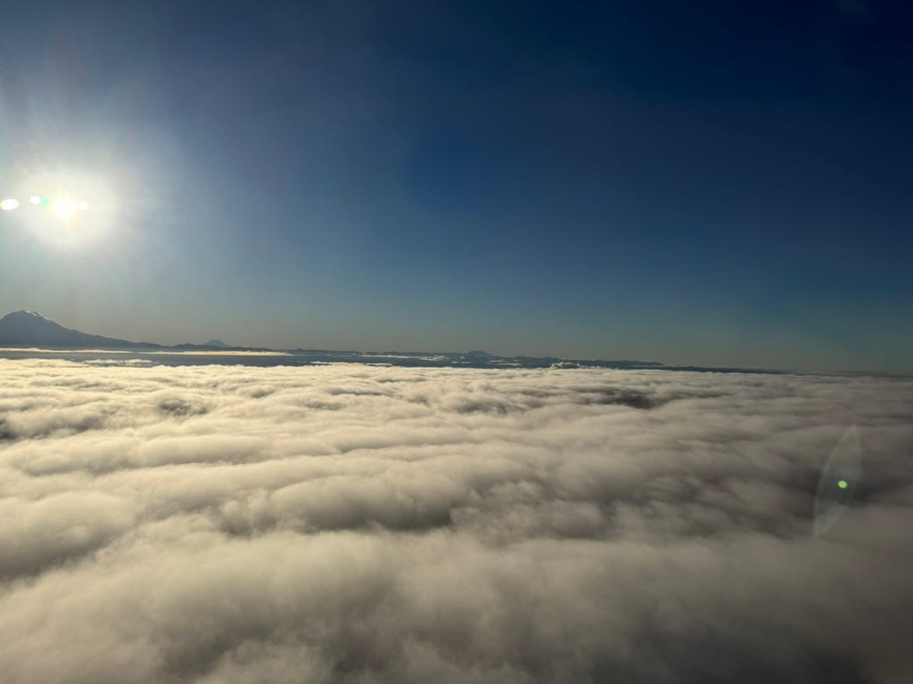 A muted, fuzzy photo above the clouds, with the bright sun in the corner, possibly from an airplane window.