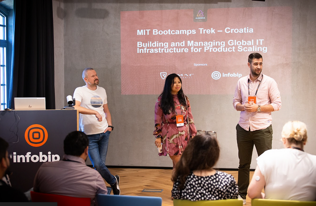 Photo of 3 adults in business casual dress presenting in front of a group of 4 visible seated audience members. Podium on the left says “infobip” and the slideshow projected on the wall behind them says “ MIT Bootcamps Trek — Croatia. Building and managing global IT infrastructure for product scaling.”