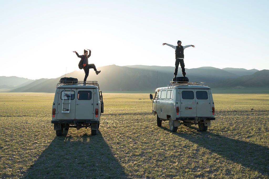 Two people looking happy on the roofs of camper vans in a field