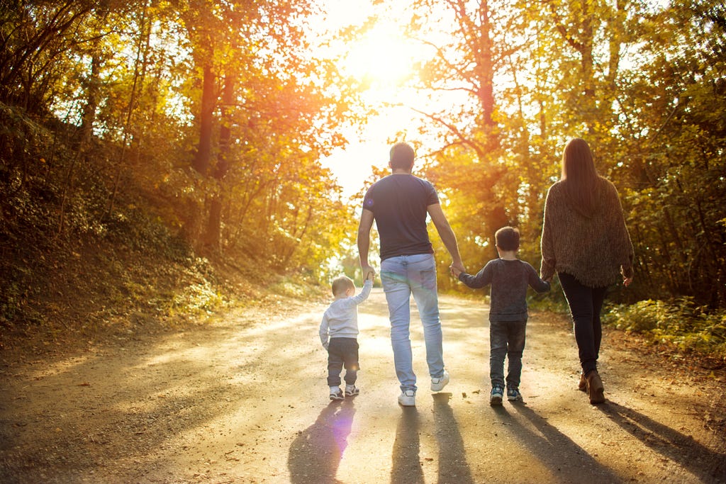 A family of four, Dad, Mom, and two kids walk down a road into the sunrise