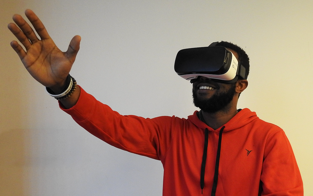 A man waves and smiles wearing a VR headset.