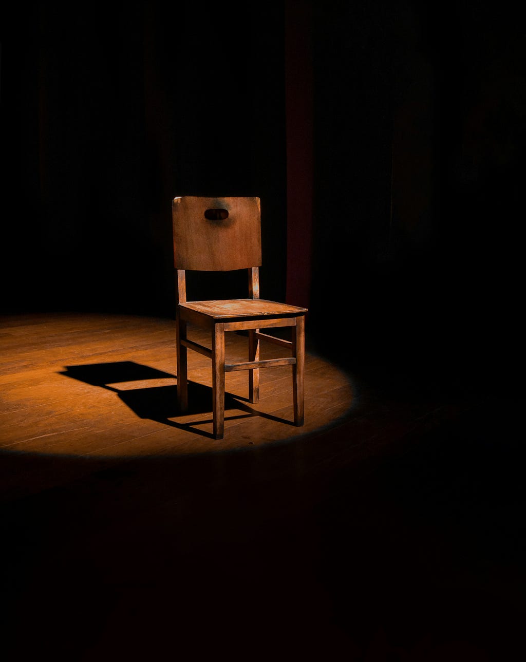 Bright light revealing a brown wooden ladderback chair while shadows lay in the surrounding space.