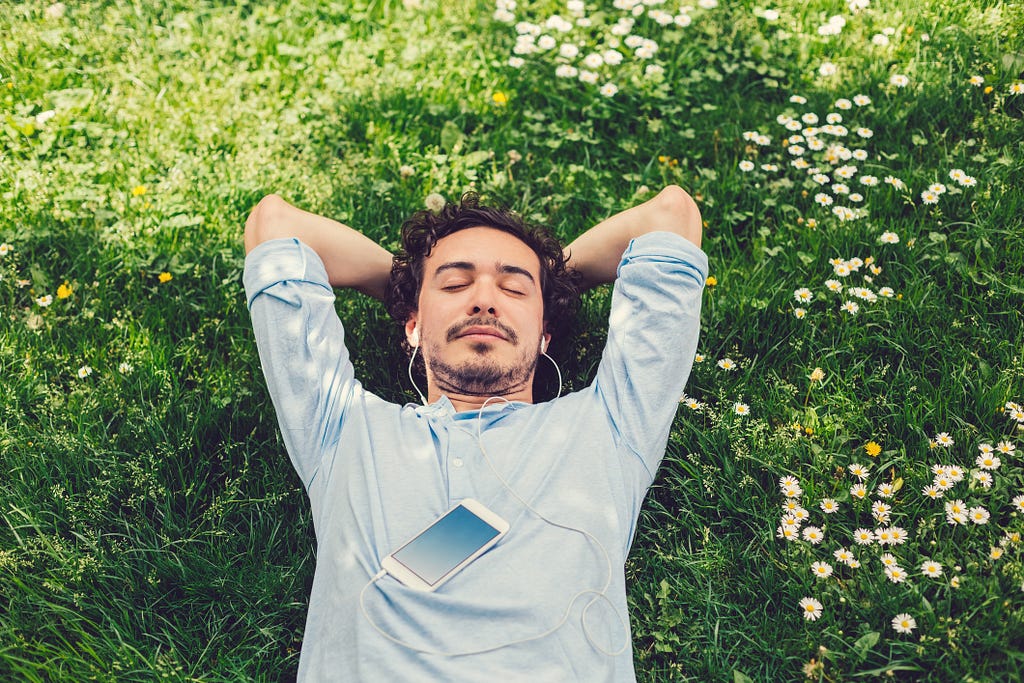 Relaxed man lying down at the meadow and listening to music