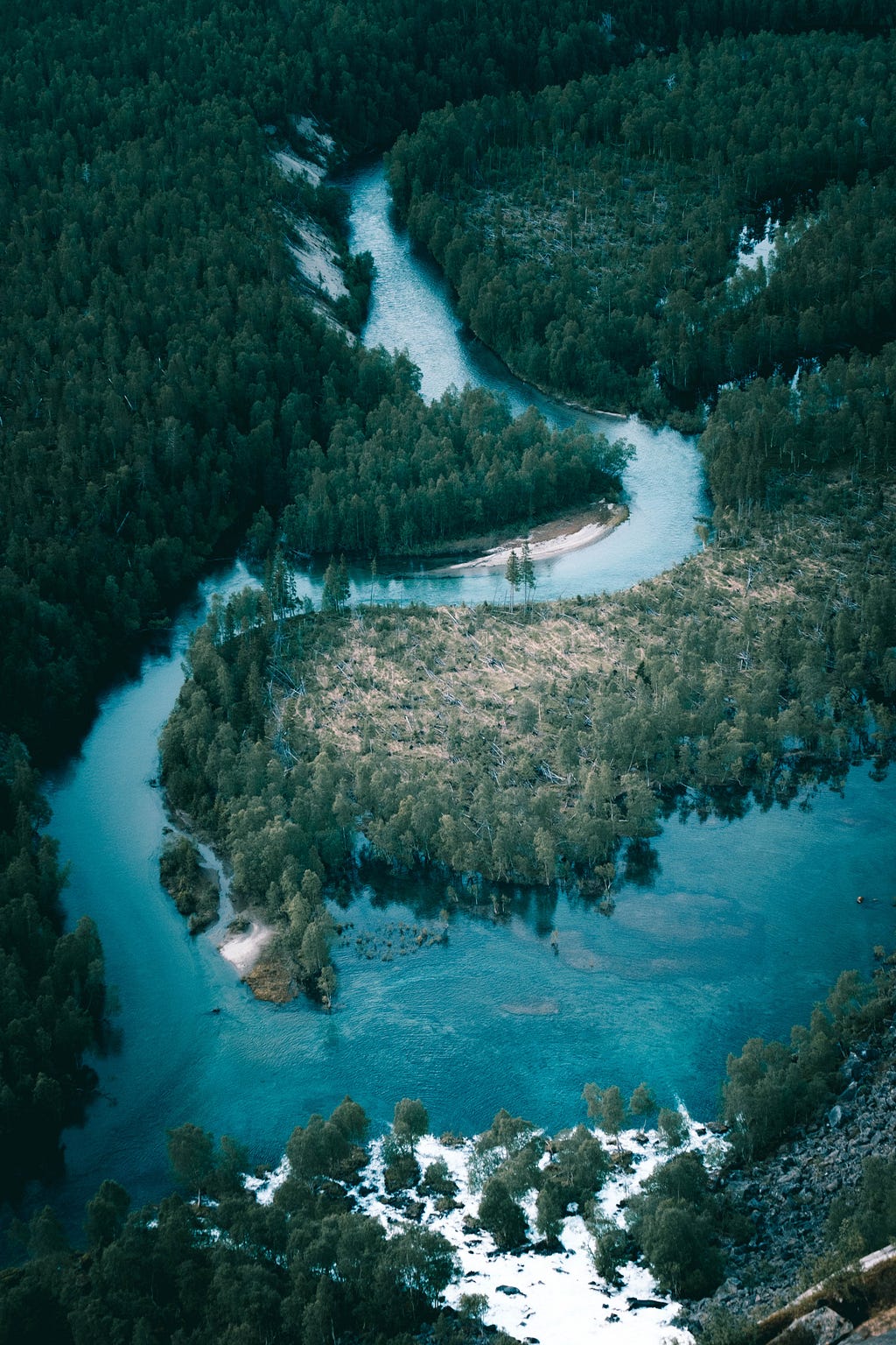 A beautiful aerial photo of a vivid blue river bordered by thick, green forests.