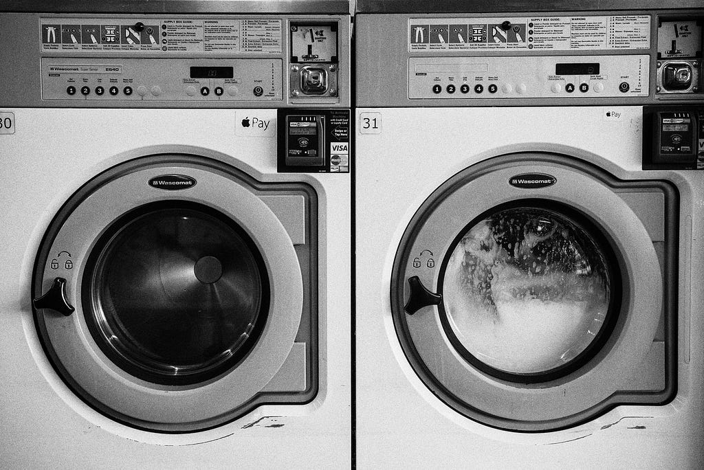 A washing machine full of clothes and suds sits next to an empty dryer