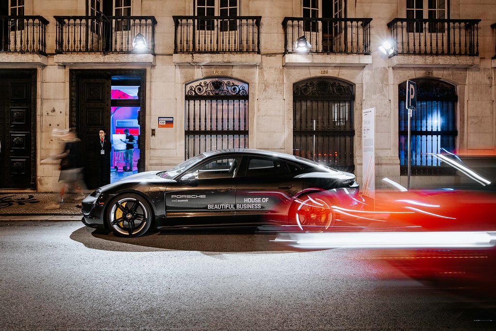 A branded Porsche Taycan in front of a historical building in Lisbon at night