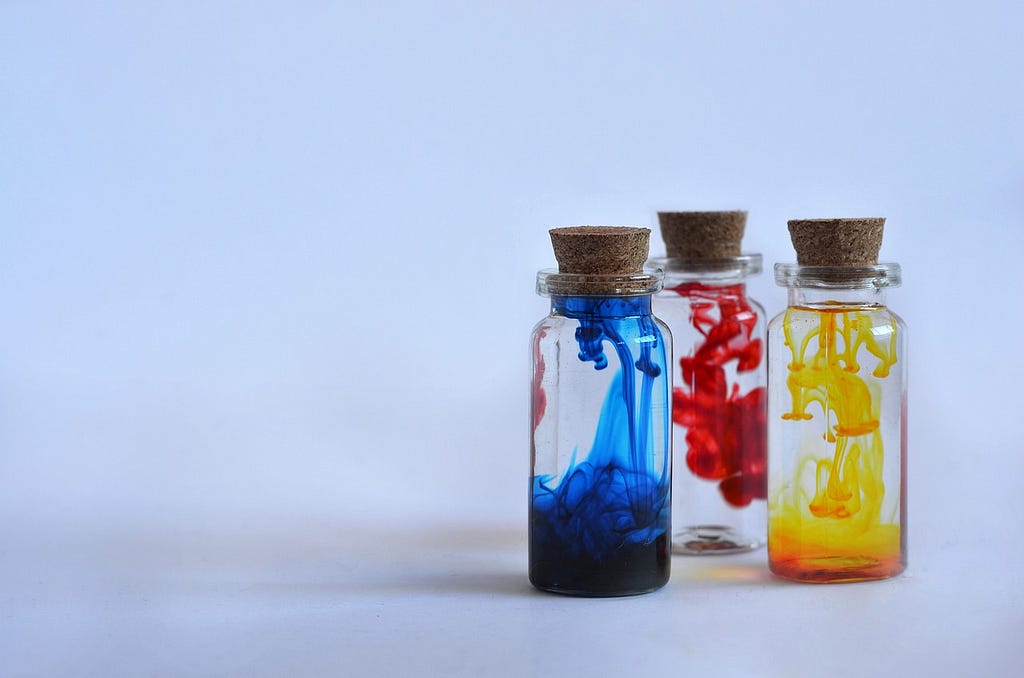 Three small flasks sealed with corks. From left to right: blue, red and yellow dye are being slowly mixed in each one.