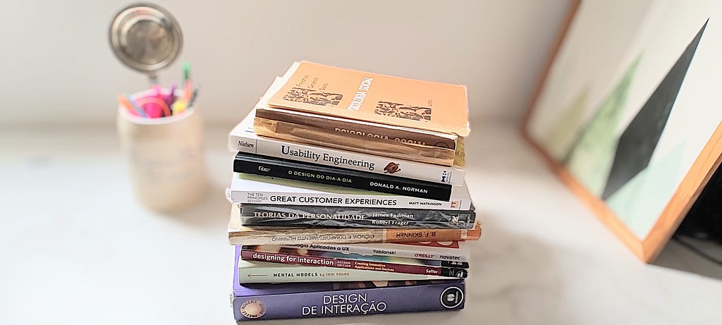 Conjunto de livros sobre ux design e psicologia empilhados sobre uma mesa de escritório branca.