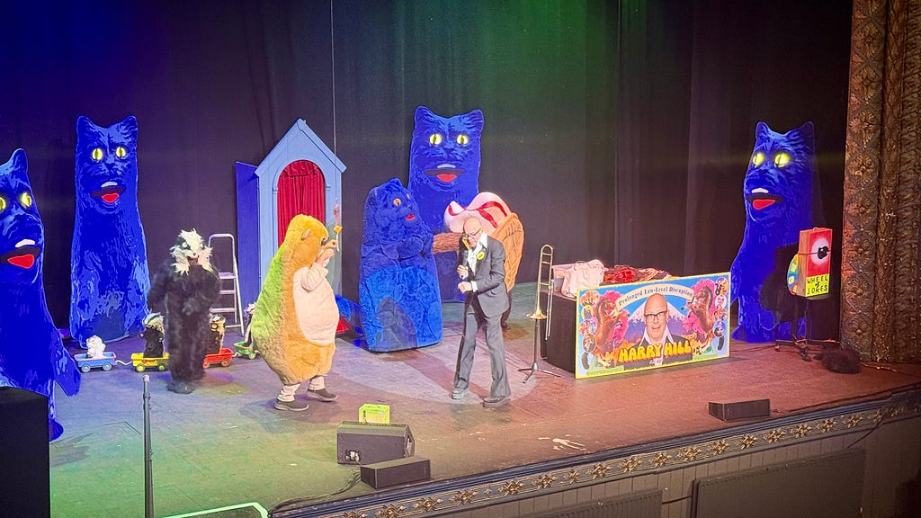 Harry Hill on stage at Newcastle’s Tyne Theatre, with an audience member dressed as a hamster, as other cast members dressed as Stouffer the Cat, a badger, and an ice cream, with a small convoy of badgers in remote controlled cars traversing the stage in the backgorund. You sort of had to be there, really …